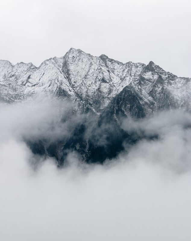 Snow-capped mountain peaks emerging from dense clouds, symbolizing breathtaking adventures and serene escapes in nature.